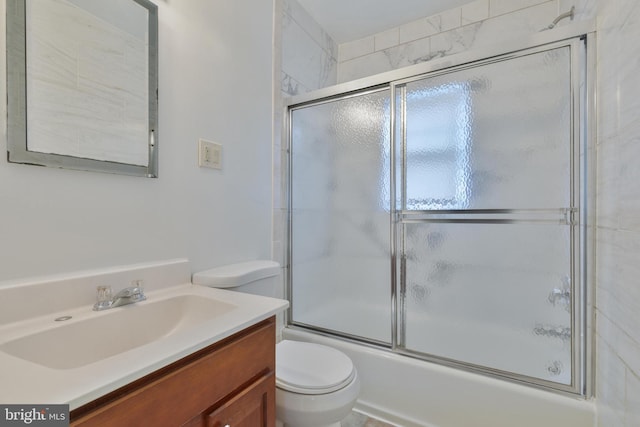 bathroom featuring toilet, shower / bath combination with glass door, and vanity