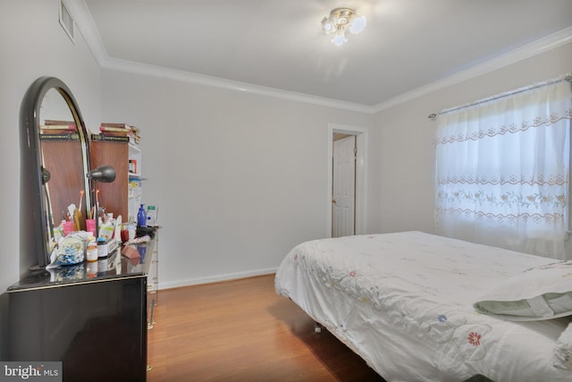 bedroom featuring ornamental molding, wood finished floors, visible vents, and baseboards