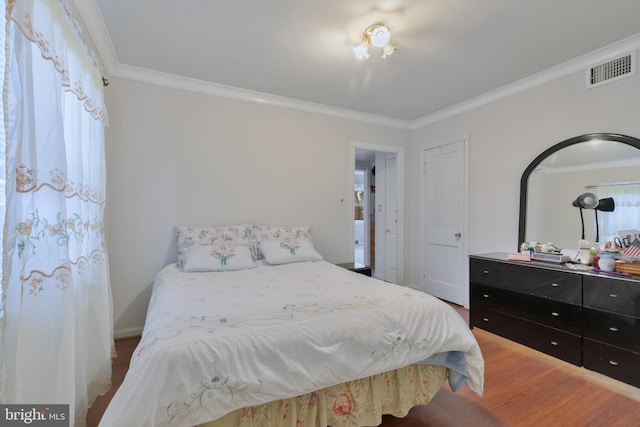 bedroom with crown molding, visible vents, and wood finished floors