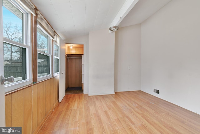 spare room featuring lofted ceiling, visible vents, wood walls, and light wood-style flooring