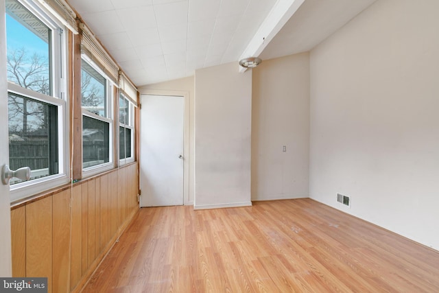 empty room with wood walls, light wood-style flooring, visible vents, and vaulted ceiling