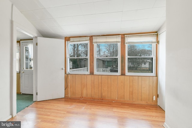 empty room with lofted ceiling, light wood-style floors, and wood walls