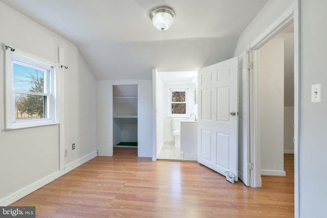 unfurnished bedroom with light wood finished floors, a spacious closet, vaulted ceiling, ensuite bath, and baseboards