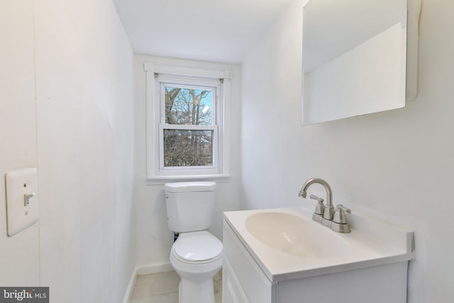 half bath with baseboards, vanity, and toilet