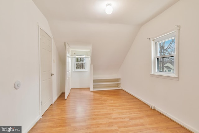 additional living space with baseboards, vaulted ceiling, and light wood finished floors