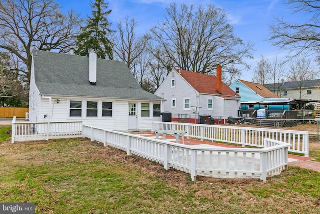 back of house featuring a shingled roof, fence, a deck, and a yard