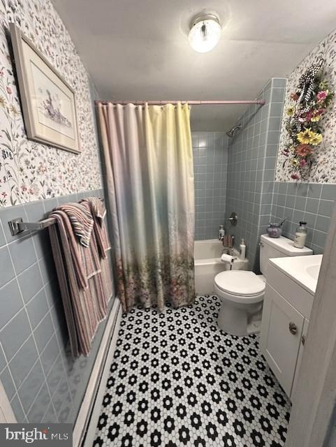 bathroom featuring a wainscoted wall, toilet, tile walls, and wallpapered walls