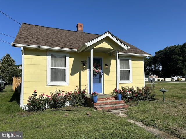 bungalow with a chimney, a shingled roof, and a front yard