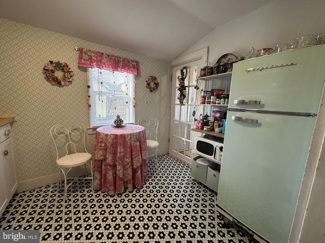 kitchen with wallpapered walls, baseboards, vaulted ceiling, freestanding refrigerator, and white cabinets