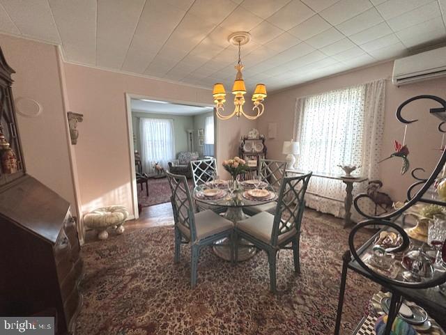 dining space with an inviting chandelier, an AC wall unit, crown molding, and wood finished floors