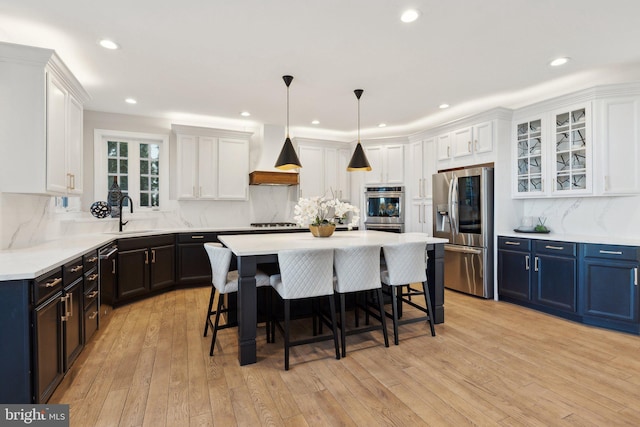 kitchen with stainless steel appliances, light countertops, white cabinetry, a kitchen island, and premium range hood