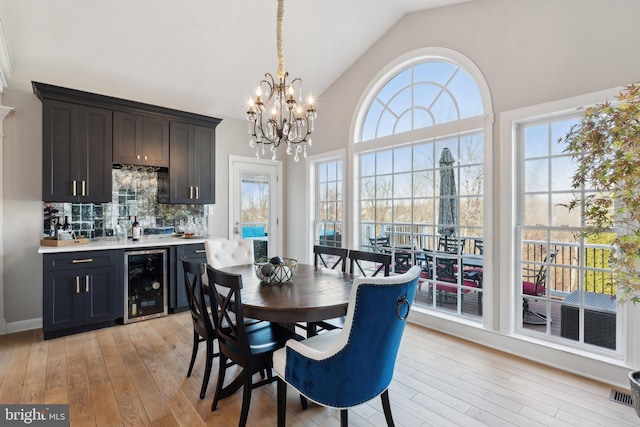 dining area featuring beverage cooler, visible vents, a chandelier, light wood-style flooring, and high vaulted ceiling