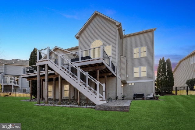 back of property at dusk featuring fence, stairway, and a yard