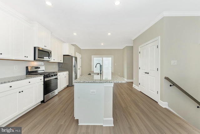 kitchen with stainless steel appliances, an island with sink, white cabinetry, and light stone countertops