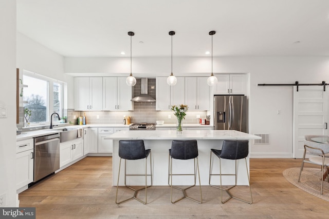 kitchen with a barn door, decorative backsplash, wall chimney exhaust hood, a kitchen island, and stainless steel appliances