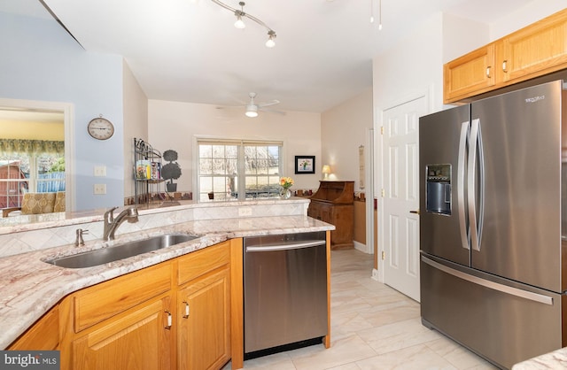 kitchen with light stone counters, stainless steel appliances, a wealth of natural light, a ceiling fan, and a sink