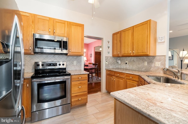 kitchen with stainless steel appliances, a sink, light stone counters, and tasteful backsplash