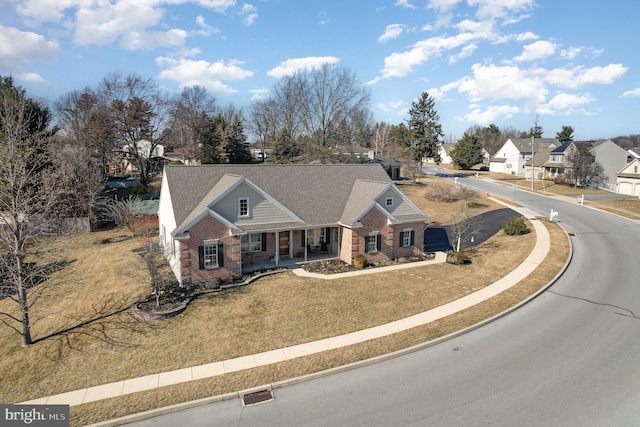 view of front of property with covered porch, brick siding, a front lawn, and a residential view