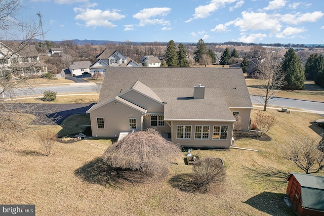 rear view of property with a shingled roof, a residential view, a lawn, and a chimney