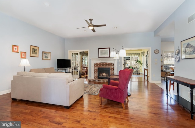 living area with recessed lighting, a ceiling fan, a brick fireplace, wood finished floors, and baseboards