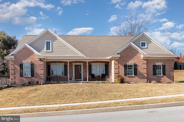 view of front of property with a shingled roof, a front yard, and brick siding