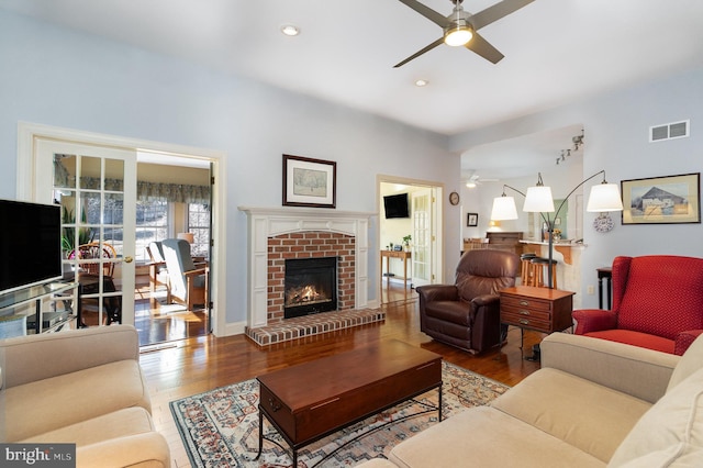 living room featuring a ceiling fan, visible vents, a fireplace, and wood finished floors