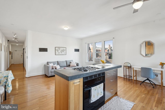 kitchen featuring light wood finished floors, a kitchen island, open floor plan, stainless steel gas stovetop, and black oven