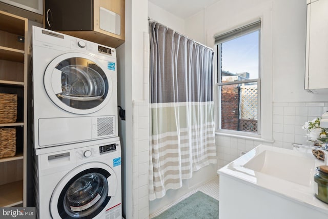 laundry area featuring stacked washer / dryer, laundry area, a sink, and tile walls