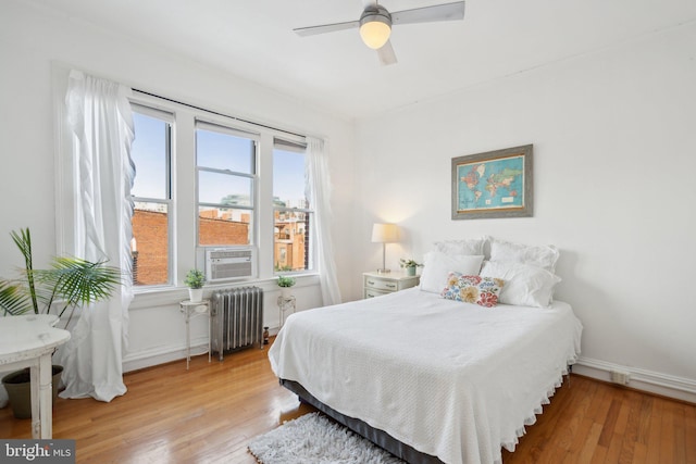 bedroom featuring ceiling fan, cooling unit, wood finished floors, baseboards, and radiator heating unit