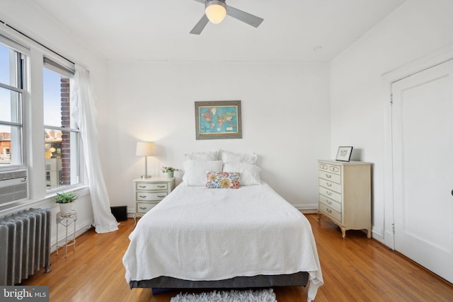 bedroom featuring light wood-style floors, baseboards, radiator heating unit, and a ceiling fan