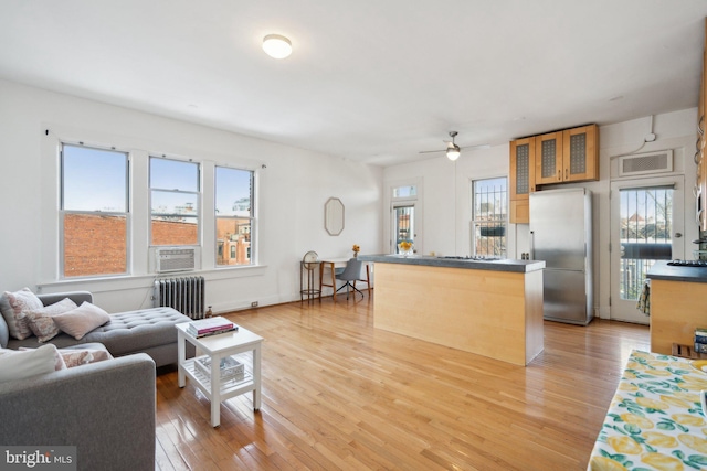 living area with a healthy amount of sunlight, radiator heating unit, cooling unit, and light wood-style floors