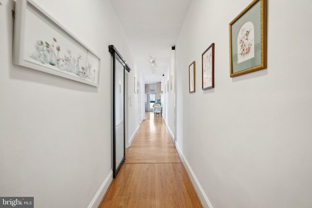 corridor with a barn door, track lighting, wood finished floors, and baseboards