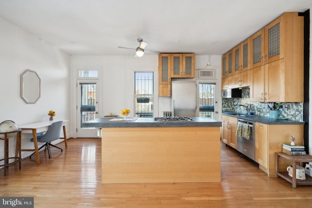 kitchen with glass insert cabinets, dark countertops, a kitchen island, and appliances with stainless steel finishes