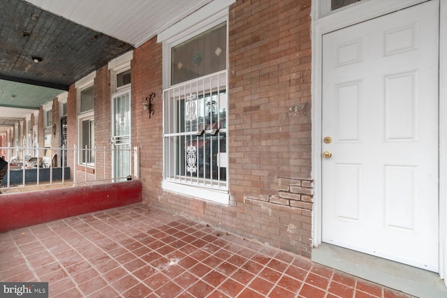 view of exterior entry with brick siding and a porch