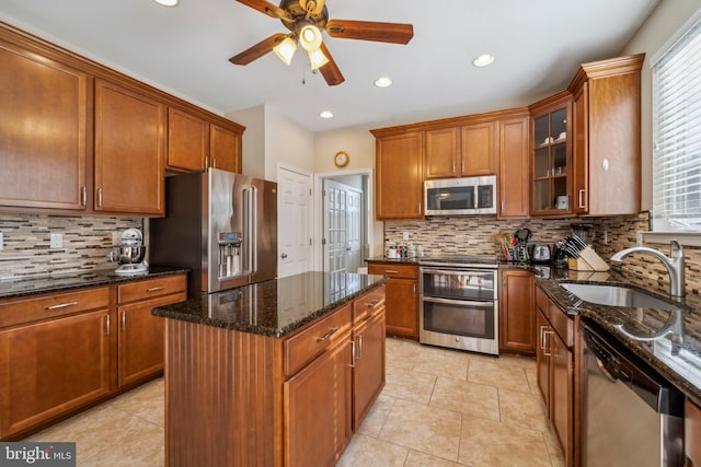 kitchen with stainless steel appliances, a sink, a center island, dark stone counters, and glass insert cabinets