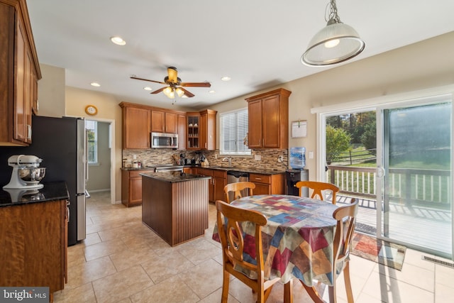 kitchen with stainless steel appliances, hanging light fixtures, brown cabinetry, and glass insert cabinets