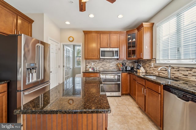 kitchen featuring dark stone countertops, glass insert cabinets, stainless steel appliances, and a sink