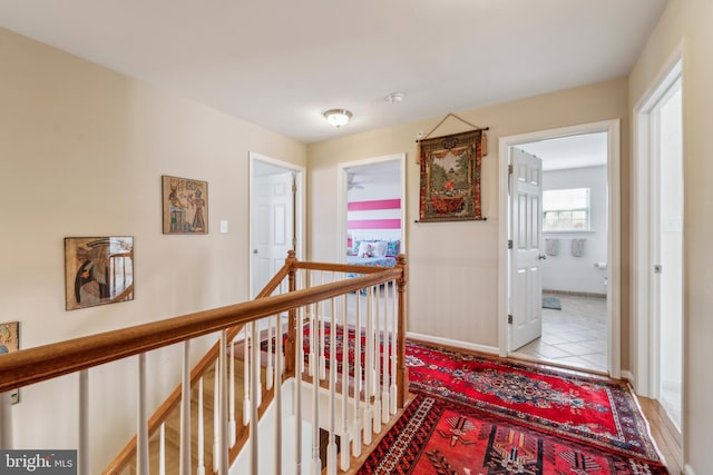 hall featuring light tile patterned floors, baseboards, and an upstairs landing