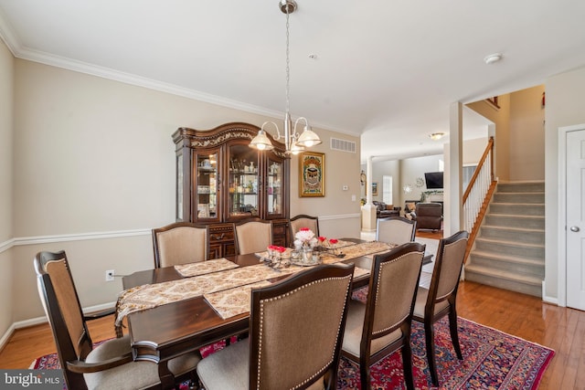 dining room featuring visible vents, stairway, an inviting chandelier, ornamental molding, and wood finished floors