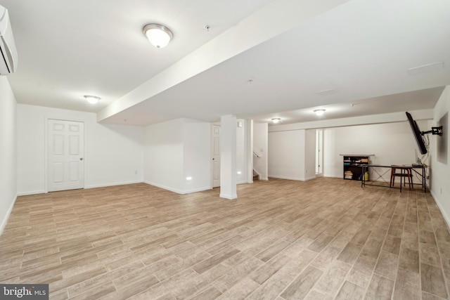 finished below grade area with stairs, baseboards, a wall unit AC, and light wood-style floors