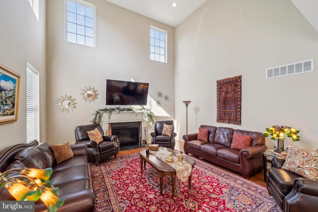 living room with high vaulted ceiling, wood finished floors, a fireplace with flush hearth, and visible vents