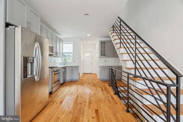 kitchen with a sink, light countertops, appliances with stainless steel finishes, gray cabinets, and glass insert cabinets