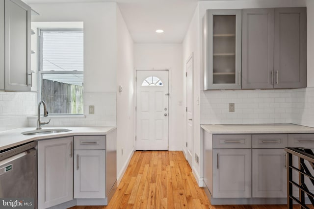 kitchen featuring gray cabinetry, a sink, light countertops, dishwasher, and glass insert cabinets