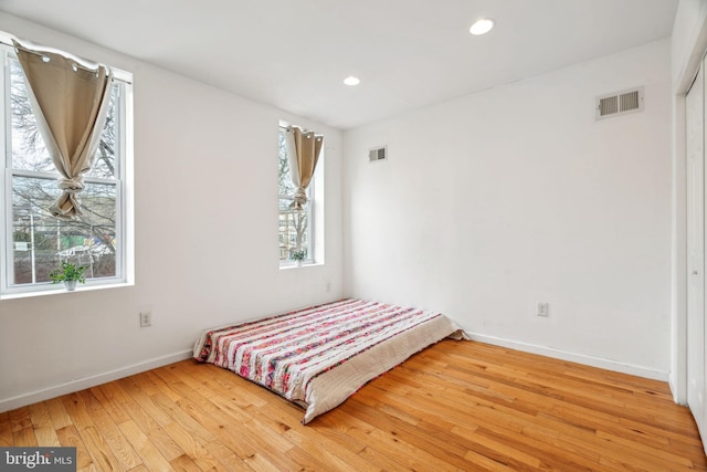 unfurnished bedroom featuring multiple windows, wood finished floors, and visible vents