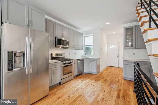 kitchen featuring stainless steel appliances, gray cabinets, light countertops, glass insert cabinets, and a sink