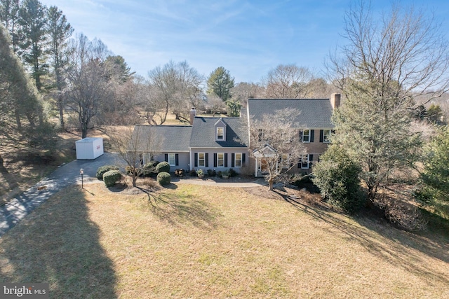 view of front of property with a shed, an outdoor structure, driveway, a front lawn, and a chimney