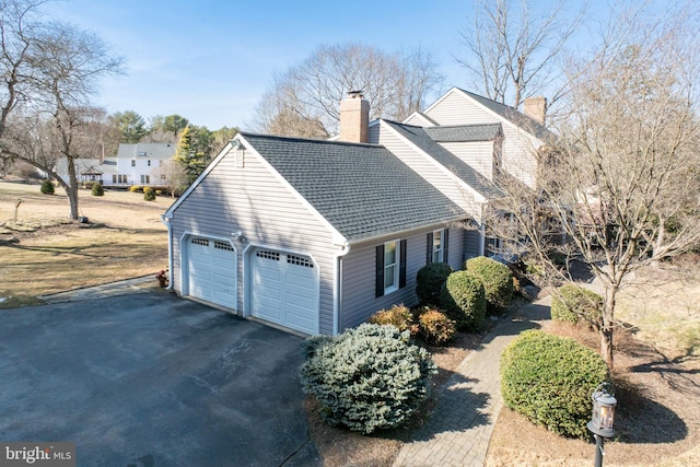 view of front facade with a shingled roof, a chimney, and a detached garage