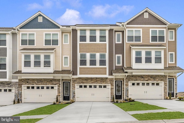 townhome / multi-family property featuring driveway, stone siding, and a garage