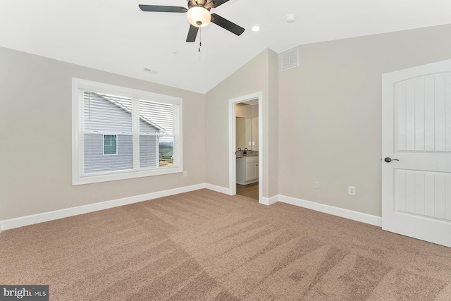 unfurnished bedroom with light carpet, baseboards, visible vents, ensuite bath, and vaulted ceiling