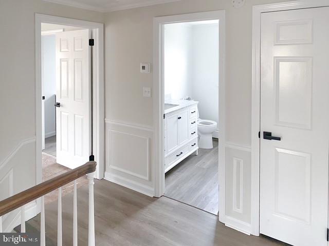 corridor with a decorative wall, light wood-type flooring, and crown molding